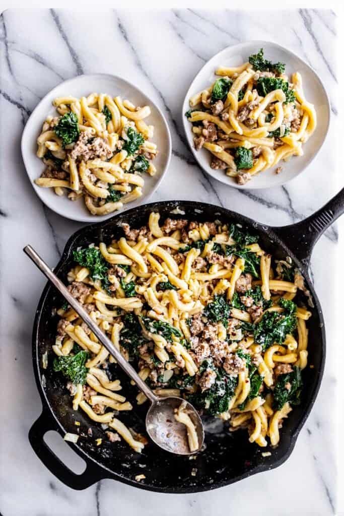sausage kale pasta on plates and in cast iron skillet