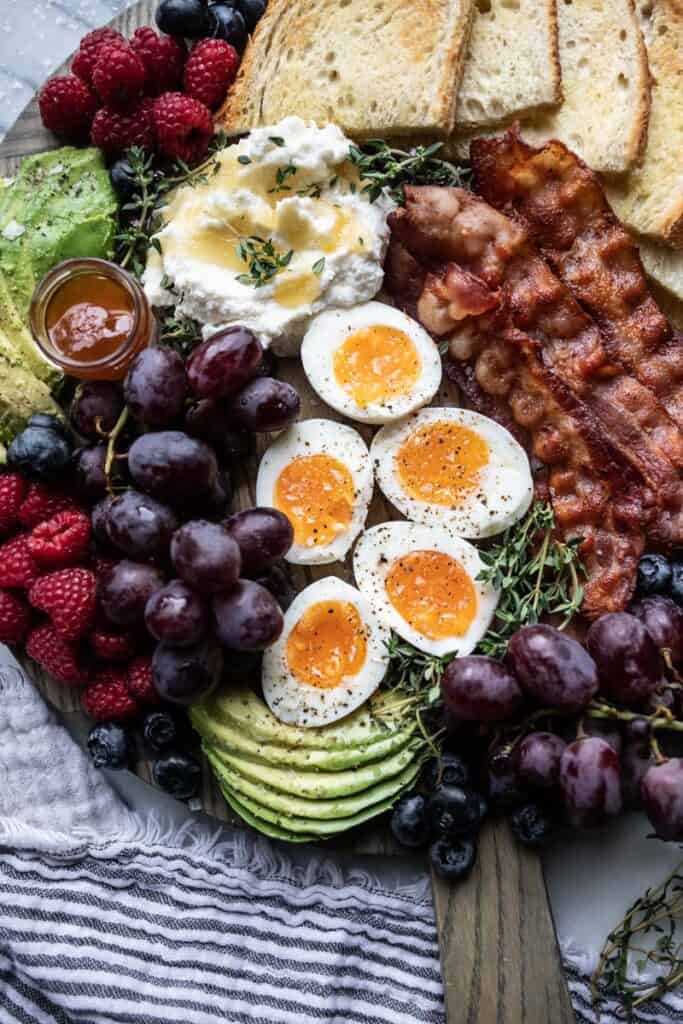 breakfast charcuterie board with bacon, soft boiled eggs, fruit, toasted bread, and whipped ricotta