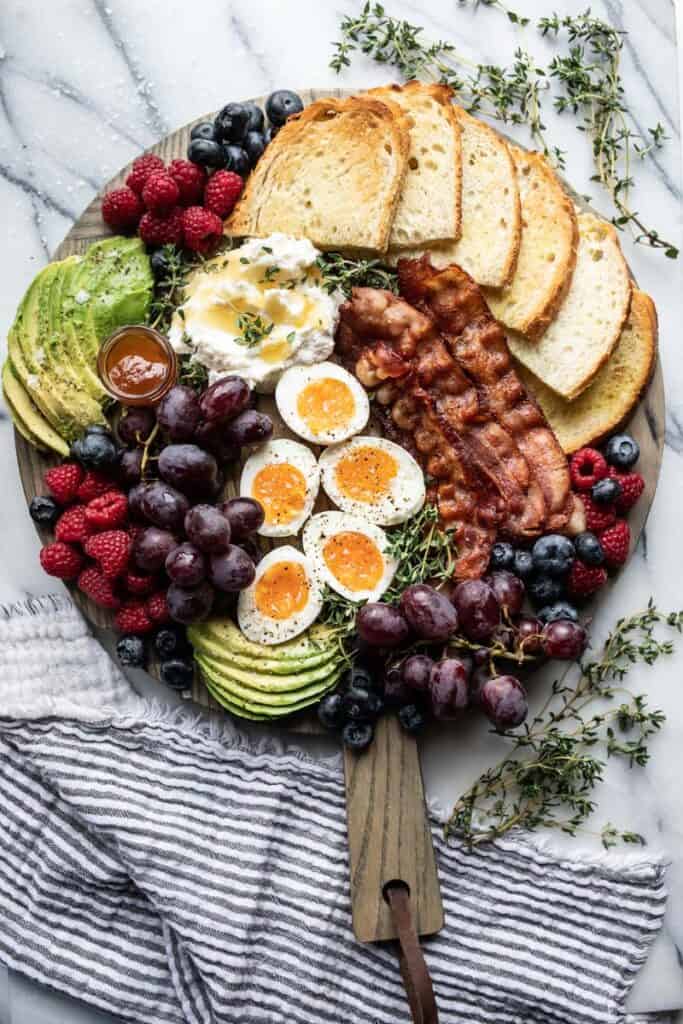 breakfast charcuterie board with bacon, soft boiled eggs, fruit, toasted bread, and whipped ricotta