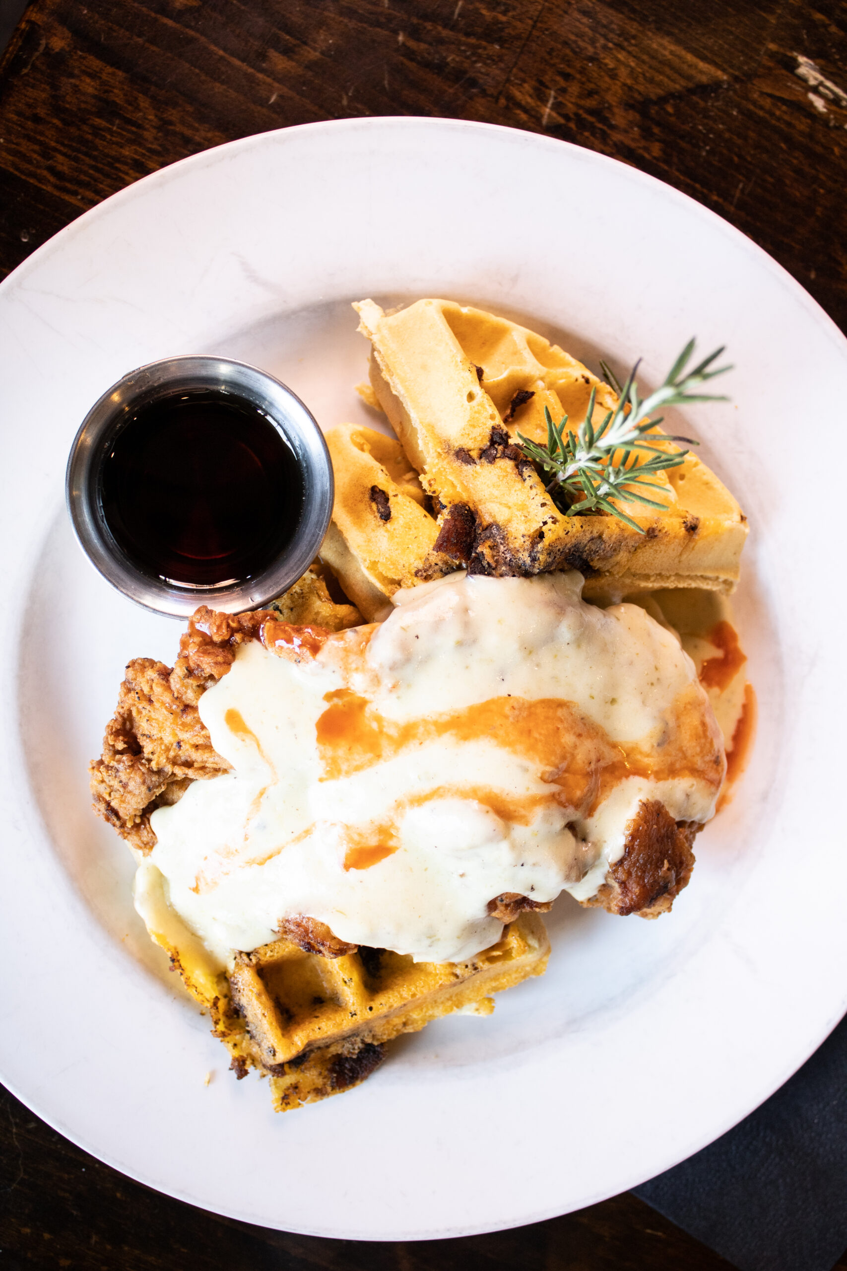 best restaurants in dallas: Breadwinners fried chicken and waffles which features jalapeño bacon cheddar waffles and crispy fried chicken sitting in a pool of cream gravy topped with hot sauce and maple syrup