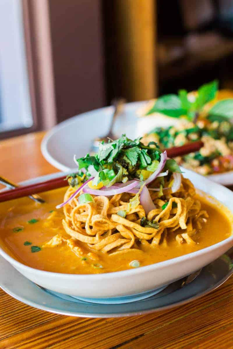 Kao Soi, a creamy curry noodle soup cooked with chicken, topped with red onion, pickled mustard greens, and crispy noodles by Pestle Rock