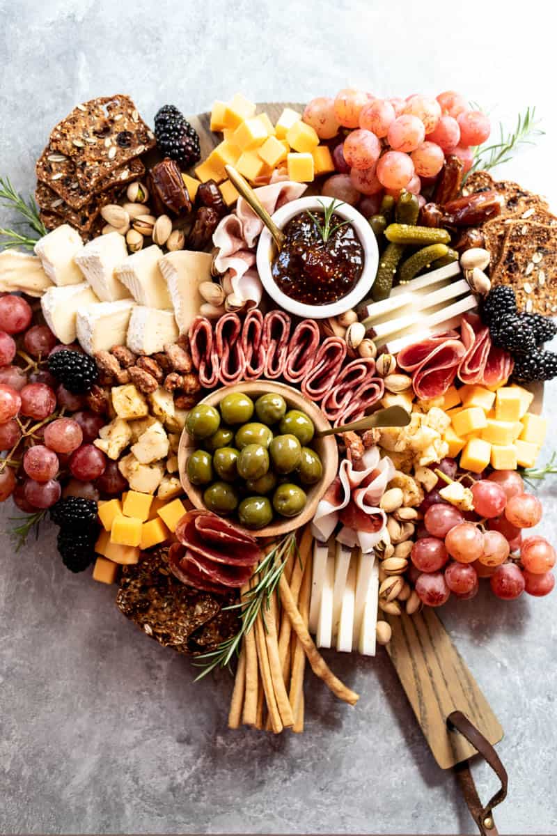cheese and meat board with olives, pickles, fruit, crackers, and nuts