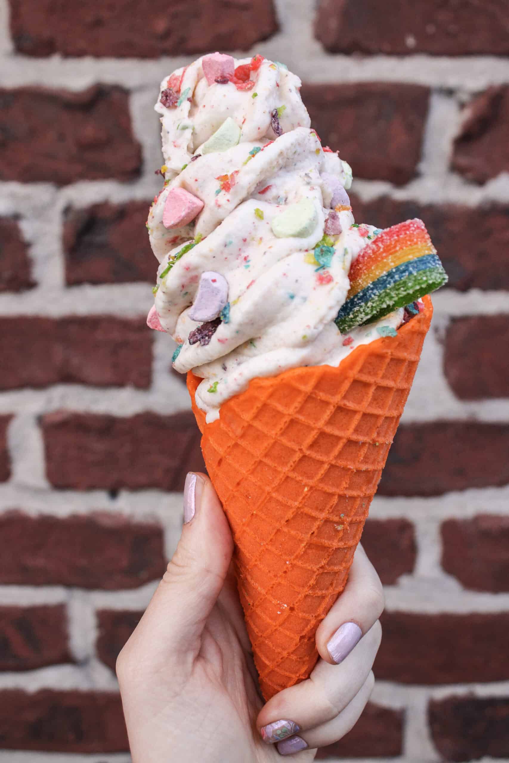 Spilled Milk's "Over the Rainbow" cone featuring Fruity Pebbles and Captain Crunch flavored ice cream, in a creamsicle cone, and topped with a rainbow sour rope
