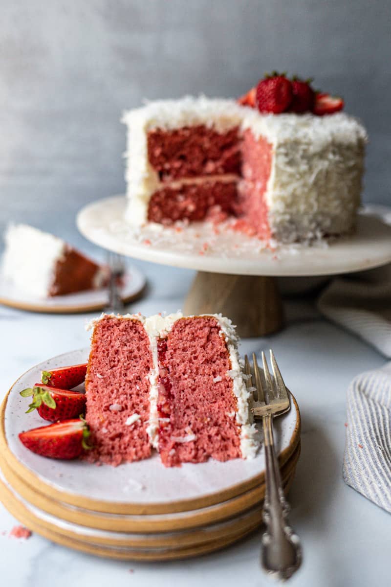 slice of strawberry coconut cake on a plate with full cake in background